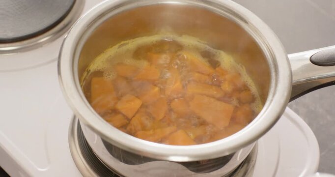 Stainless-steel saucepan on kitchen hob heating water, orange cubes bubbling and softening