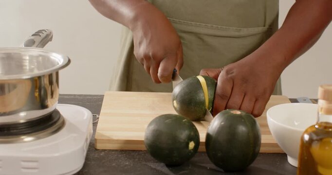 Man in green apron grabbing knife and spoon, cutting, scooping melon on cutting board for cooking