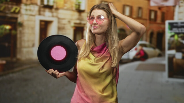 Woman holding vinyl record with hand on head and pink sunglasses on a cobbled street; nostalgia retro.