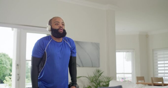 African American man taking breath lifting hex weights at home wearing headphones building strength