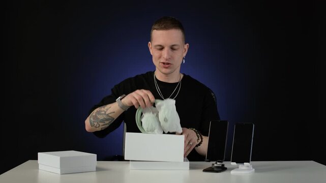 Static shot of young blogger breaking into smile while presenting newly released headphones, taking it from box