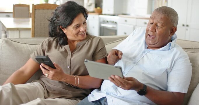 Man tapping tablet, showing content, woman leaning in and smiling while holding phone on sofa