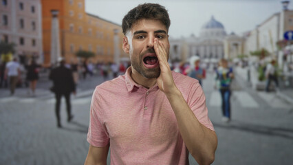 Obraz premium Hispanic man wearing pink shirt opens mouth and clenches fists beside building; triumph excitement.