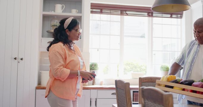 African American couple unpacking wooden crate of produce in home kitchen, woman using smartphone