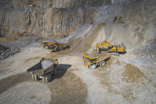 Aerial view of heavy machinery including excavators and dump trucks operating in an open-pit mine with steep rocky walls in Santa Lucia de Gordon, Castile and Leon, Spain.