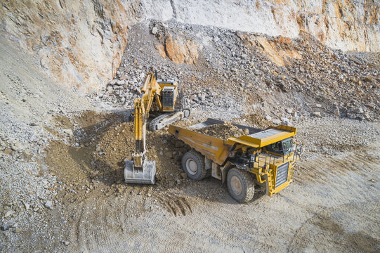 Aerial view of a yellow excavator loading a large dump truck in an open-pit mine with rocky cliffs in Santa Lucia de Gordon, Castile and Leon, Spain.