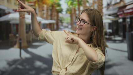Fototapeta premium Woman pointing finger at urban street café scene with raised arm gesture showcasing glasses and casual style; confidence.