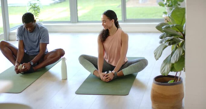 African American pair arriving studio in gymwear on mats stretching man reaching feet woman smiling