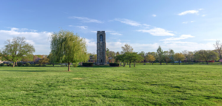 Panoramic view of the historic Joseph Dill Baker Carillon tower in Baker Park, Frederick, Maryland, surrounded by a lush green lawn under a clear blue sky.