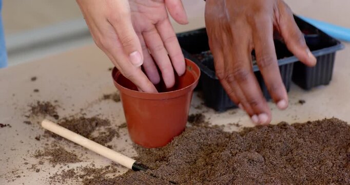 Man and woman scooping from loose potting mix, shaping soil puck, placing into pot for propagation