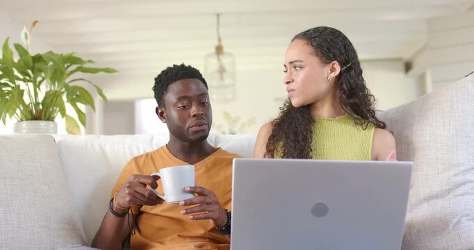 African American couple sitting on couch, woman scrolling laptop, man holding mug asking to clarify