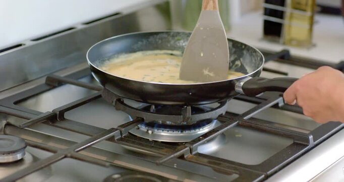 African American man stirring mixture using spatula in nonstick pan on lit gas burner, thickening