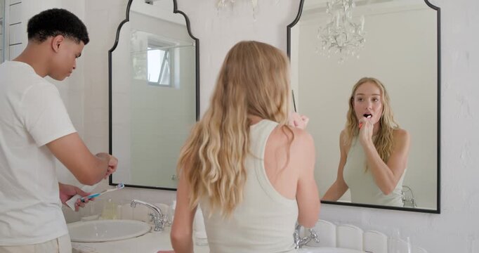 Couple at double vanity, sunlight signaling, squeezing toothpaste onto toothbrushes and brushing