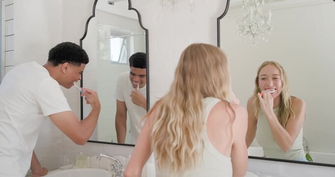 Couple starting morning routine brushing teeth with toothbrushes at bathroom vanity mirror