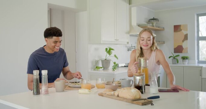 Couple starting breakfast at kitchen island as woman pouring orange juice, man cutting bread