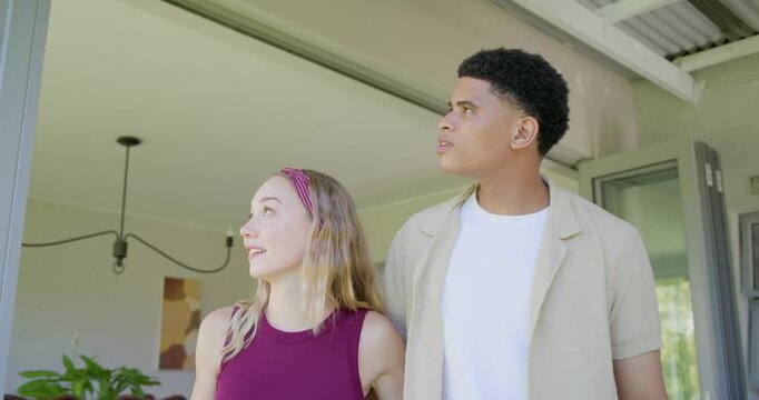 Diverse couple at glass door spotting outdoors, pointing, leaning, waving red-tag keys celebrating