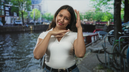 Fototapeta premium Woman with hands raised and hand near head on street beside amsterdam canal; joyful travel memory moment.