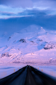Distant view of a car driving along an Empty straight road with a snowy mountain backdrop, Vatnajokull National Park, Iceland