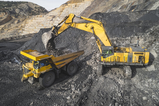 Aerial view of a large yellow excavator loading coal into a heavy-duty dump truck in an open-pit mine in Santa Lucia de Gordon, Castile and Leon, Spain.