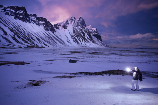 Side view of a young Woman standing in a snowy winter landscape holding a torch, Hofn, Hornafjordur, Iceland