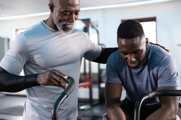 African American men training in gym, Senior coach wearing gray sleeves guiding client on air bike © wavebreak3