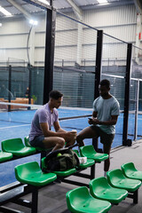Sitting and standing two players in athletic shirts chatting at court, green seats, duffel, phone © wavebreak3