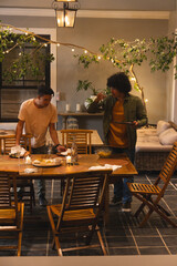 Male friends standing by wooden dining table on covered patio, holding plates and lifting glass © wavebreak3