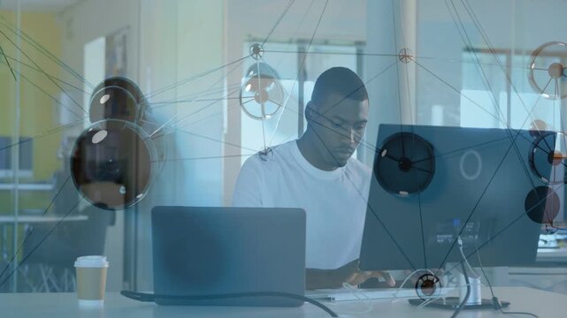 Mid-adult man typing at desk and starting network overlay, technology data mapping across monitor