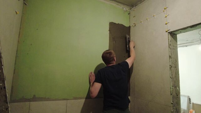 A person works on applying plaster to a wall in a living room during a home renovation project. Tools are visible as the task continues in a residential space.