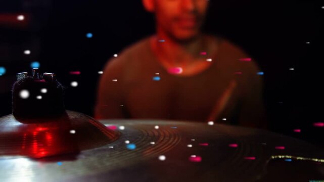 Drummer striking cymbal with drumstick entering frame for music, particles drifting across kit