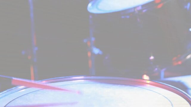 Drumstick striking tom head, sending cymbal tilting and tom vibrating during live music performance