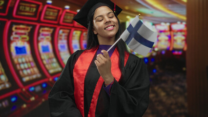 Obraz premium Woman with mortarboard holding finland flag by a row of slot machines in a casino hall; achievement pride.