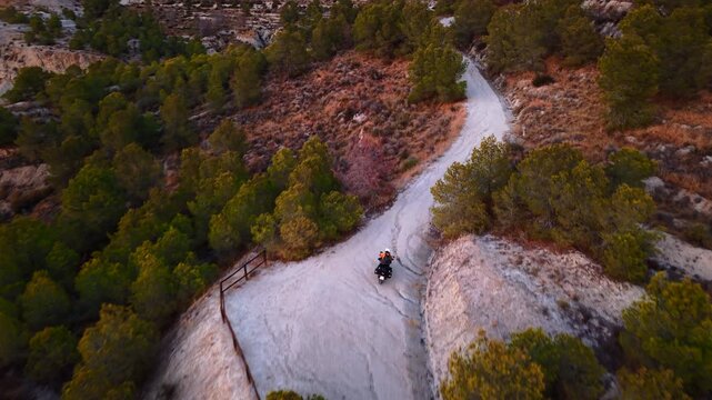 Aerial view of a motorcycle riding on a winding dirt road at sunset