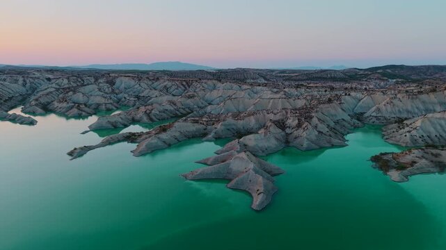 Aerial view of badlands and turquoise reservoir water during a scenic sunset