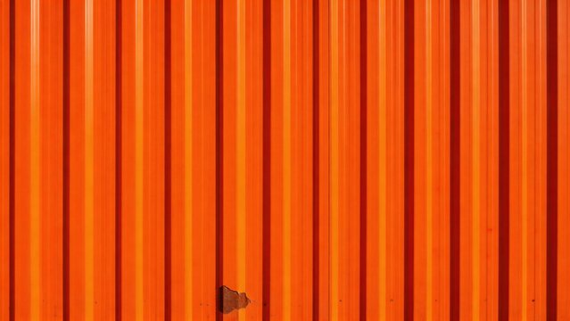 A close-up view of a vibrant orange corrugated metal wall with a rusty hinge, showcasing its textured surface and industrial design.