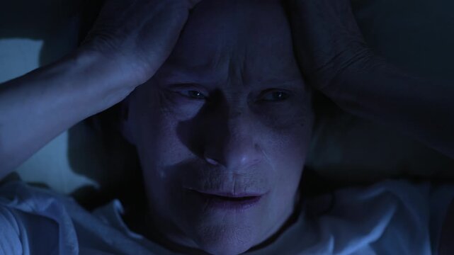 Elderly woman suffering from migraine lying in bed at night