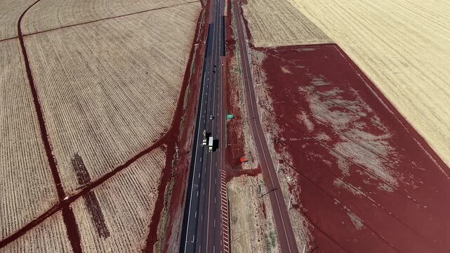 Aerial drone view of agricultural farmland with highway and intersection showing logistics flow, crop fields and rural transport infrastructure.