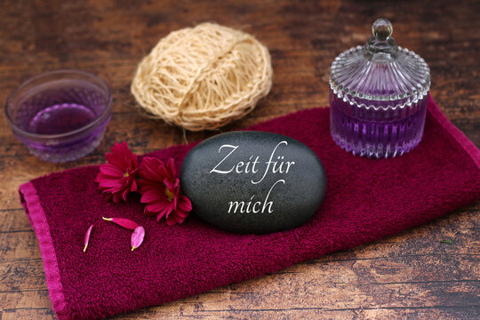 Stein mit Schriftzug 'Zeit f&uuml;r mich' auf beerenfarbenem Handtuch mit Aroma&ouml;l.&ldquo;
