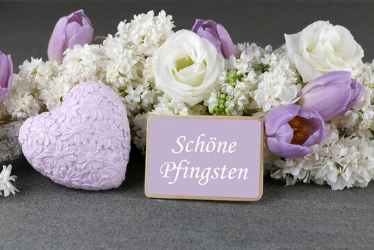 Gru&szlig;karte Sch&ouml;ne Pfingsten: Stillleben mit wei&szlig;em Flieder, Tulpen und violettem Herz mit Schriftzug 'Sch&ouml;ne Pfingsten'.&ldquo;
