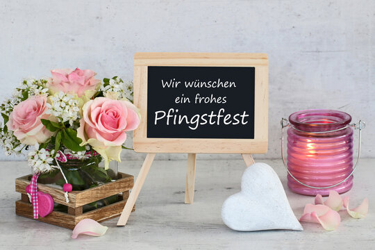 Herzliche Pfingstgr&uuml;&szlig;e: Stillleben mit Rosen, brennendem Windlicht und Tafel  mit dem Text Wir w&uuml;nschen ein frohes Pfingstfest.