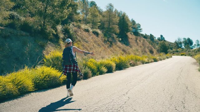 Young woman walking and hitchhiking on an open mountain road, symbolizing freedom, independence and life journey. Concept of escape, change and personal direction in life.