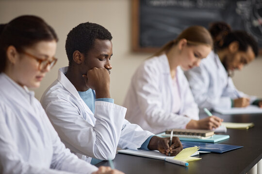 Multiethnic medical students taking notes during classroom training, preparing for healthcare careers and clinical exams. Useful for education marketing, medical school promotion