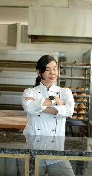 Vertical video: Mid adult chef opening eyes folding arms preparing to serve bread at marble counter