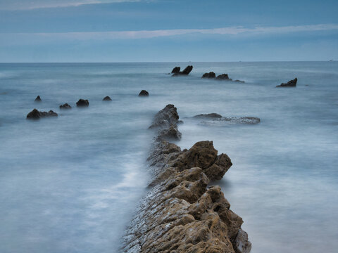 Striking Flysch Rock Leading Line Blue Hour Coast - Dramatic long exposure of a solitary flysch rock formation acting as a leading line towards the mountains under a cool blue hour sky.