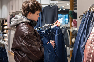 Fototapeta premium Teen boy shopping for new clothes in store, fashion and modern lifestyle. Young man selecting clothes on rack in store, retail shopping and style choice
