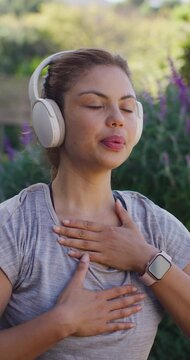 African American woman breathing in park among purple flowers, wearing gray tee, headset and watch