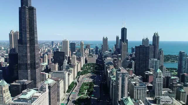 Expansive aerial video of Chicago cityscape on a crystal-clear sunny day. Willis Tower towers among gleaming modern skyscrapers and classic landmarks, highways teeming with traffic to Lake Michigan.