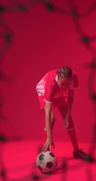 Controlling teen soccer player juggling ball in red studio wearing striped jersey, blurred net