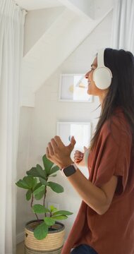 Vertical video: Woman by tall window, music starting, swaying and adjusting white headphones