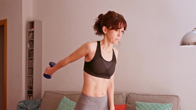 Fit middle aged woman doing triceps dumbbell kickbacks at home